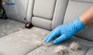 Hand using a rubber glove to clump dog hair on a car seat.